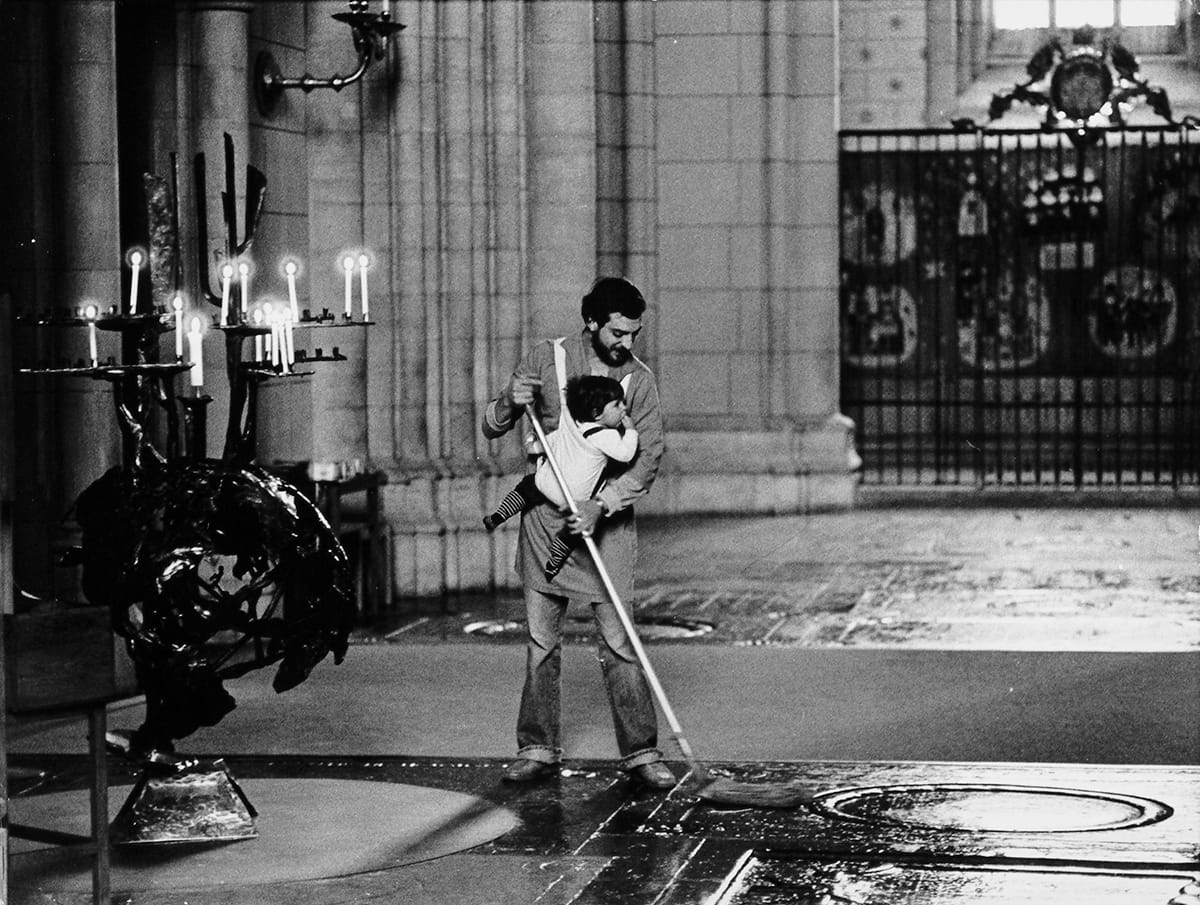 A man mops the floor with a baby strapped to his chest at a cathedral