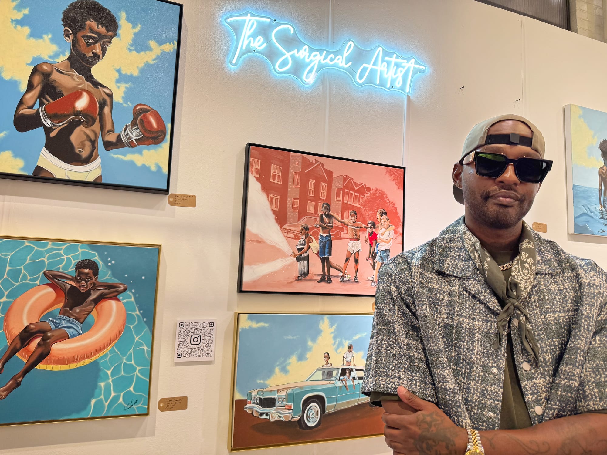 Artist Darryl Cumbie, known as The Surgical Artist, stands in front of his nostalgic paintings depicting scenes of  childhood at The Other Art Fair in Brooklyn