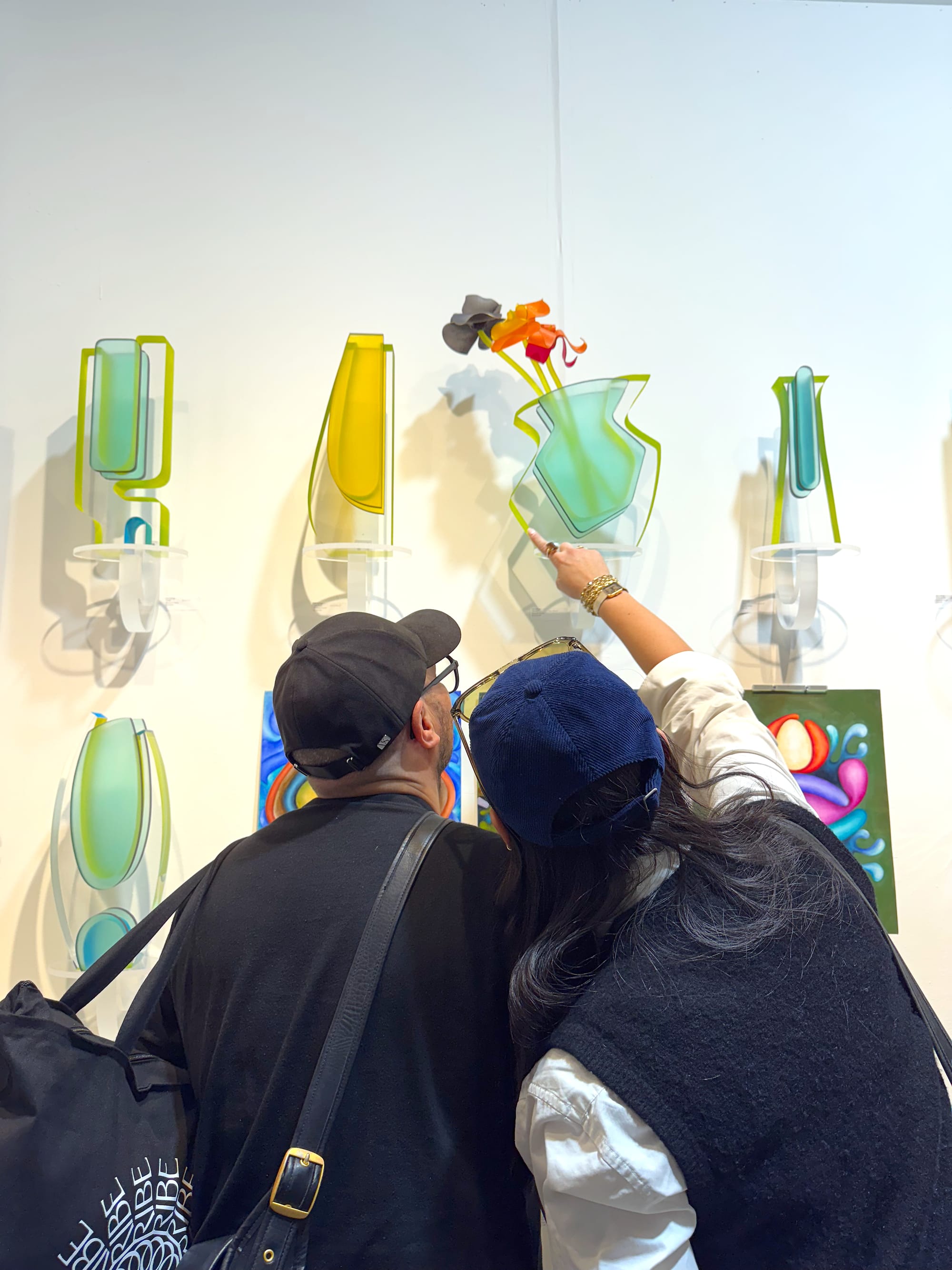 Two visitors examine colorful vase sculptures displayed on a wall at The Other Art Fair in Brooklyn.