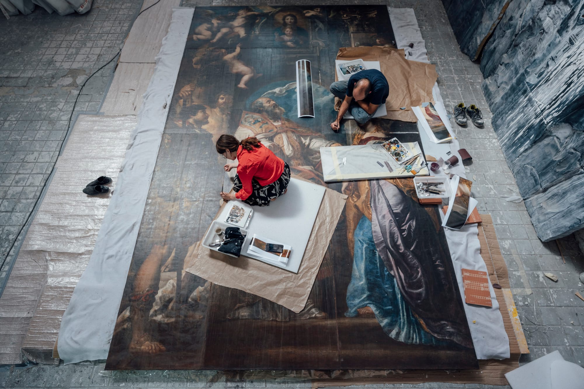 Conservators restoring a large historical painting in a Madrid art conservation studio.