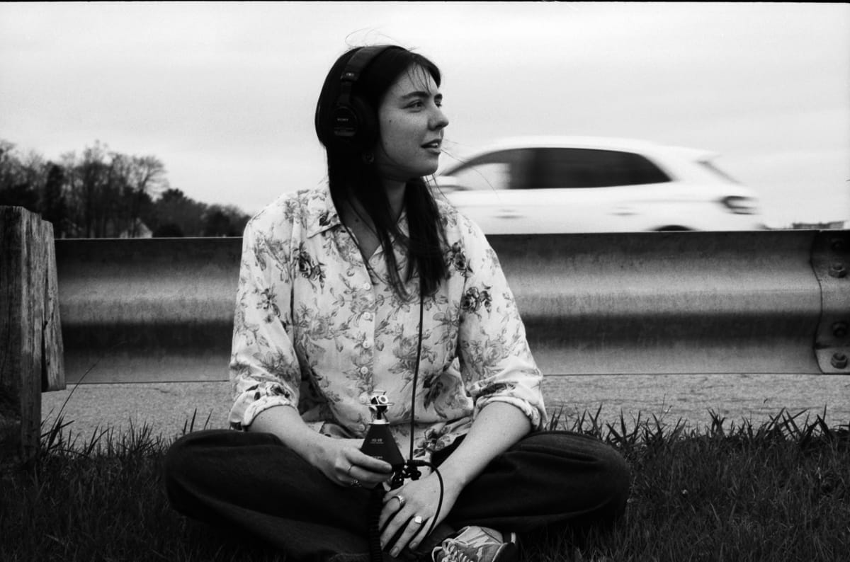 A black and white portrait of artist Anne E. Stoner as a car moves in the background