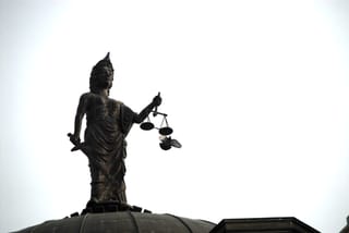 A bird flies past the scales of Lady Justice atop a courthouse dome