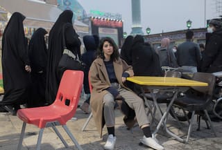 An Iranian woman sits on a chair in a busy square in Tehran, defying the mandatory hijab law