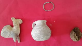 Three small antiquity-like objects displayed on a red clot  with a thin greenish metal bracelet or ring positioned above them.