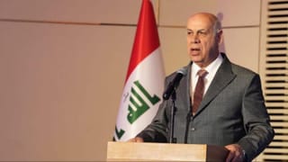 A man stands at a podium with the Iraqi flag behind him