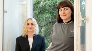 Portrait of Salome Vakhania and Natia Bukia posing by a large open window with a view of green trees