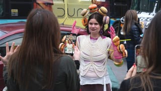Artist Vita Kari wears a performance costume while being photographed by onlookers on a city street.