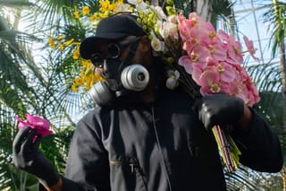 Mr. Flower Fantastic is pictured holding an orchid while wearing a mask. 