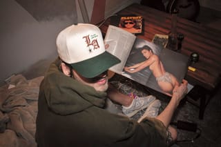 A young man looks at a playboy magazine with drug paraphernalia on the table in front of him