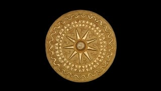 Gold disc pendant from the Asante region of Ghana is seen against a black background