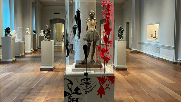 Red and black paint is seen smeared on the enclosure and pedestal of a sculpture of a little girl