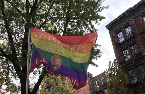 A rainbow flag with the Stonewall National Monument Established 2016 with the NPS arrowhead flying in Christopher Park